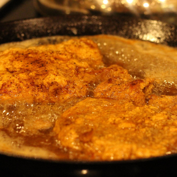 southern fried pork chops frying in iron skillet on stove