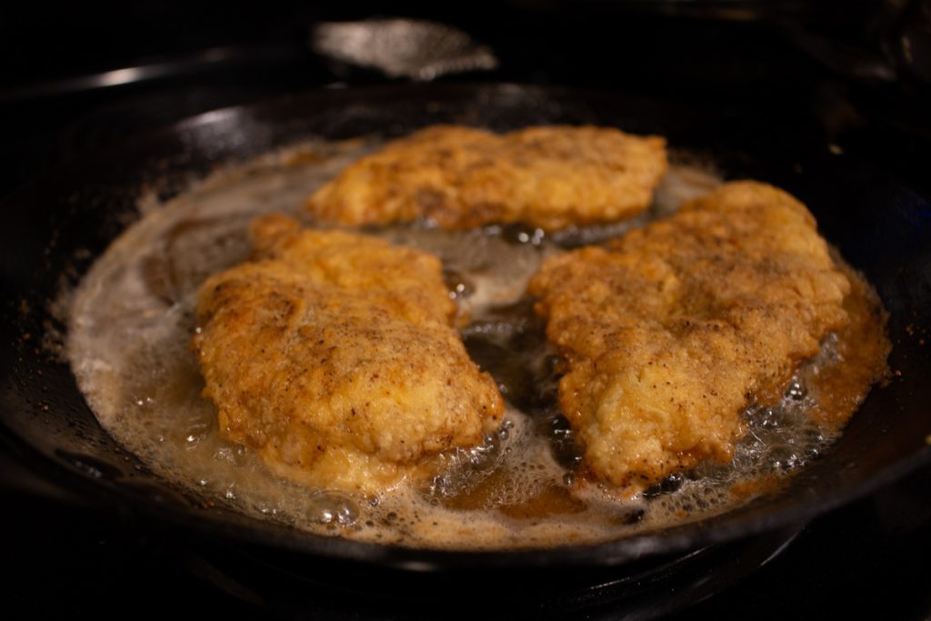 fried chicken in oil on stove in iron skillet