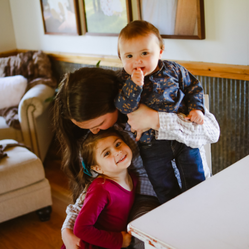 mother hugging daughter and son at kitchen table