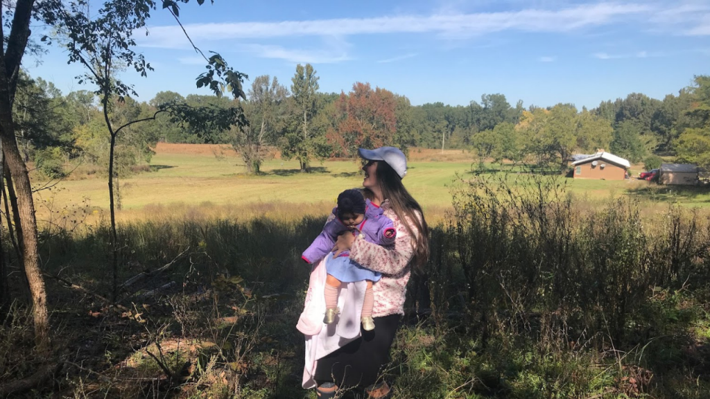 mother holding baby on farm land overlooking house in field